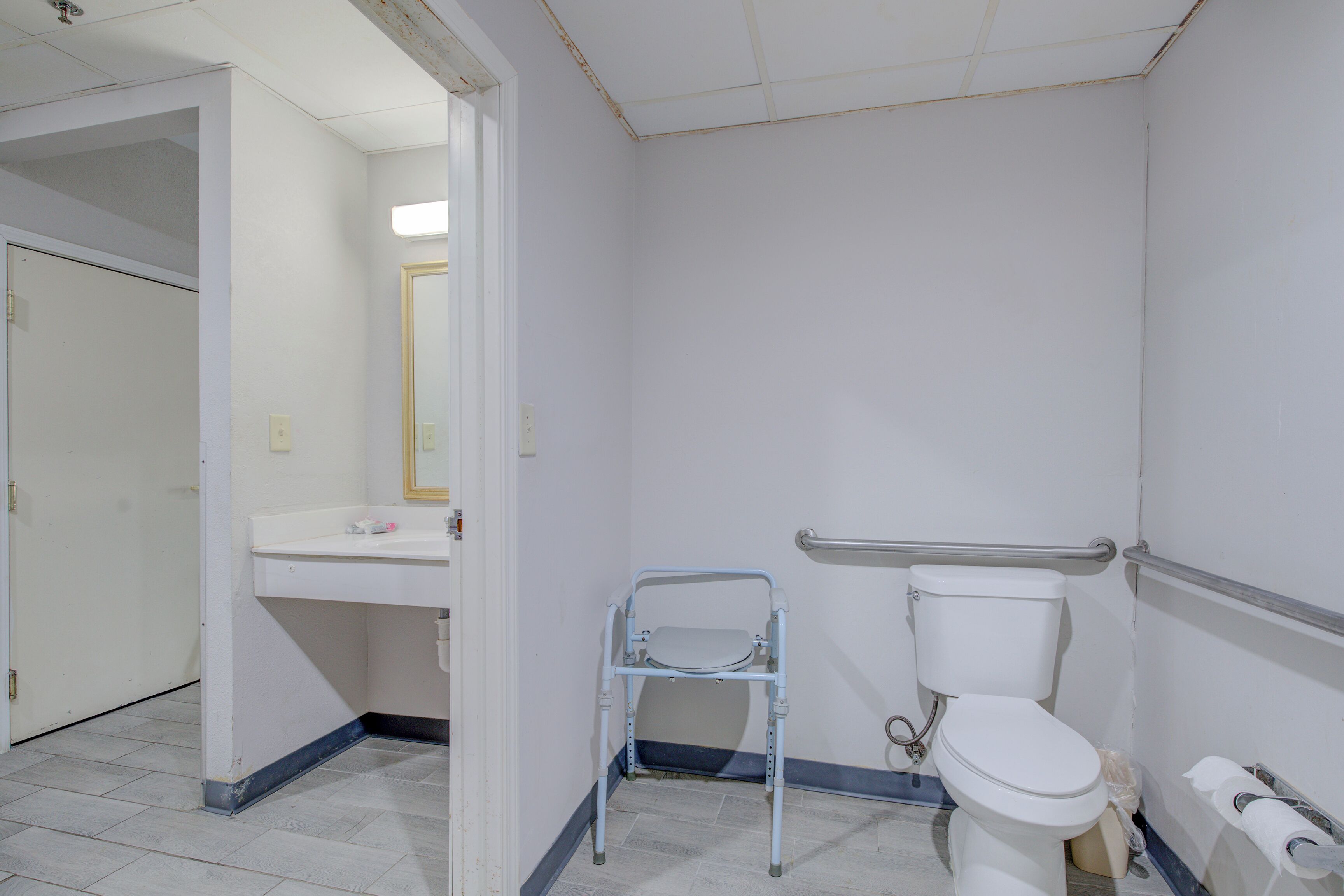 A bathroom with a toilet, a handrail, a sink, and a wheelchair.