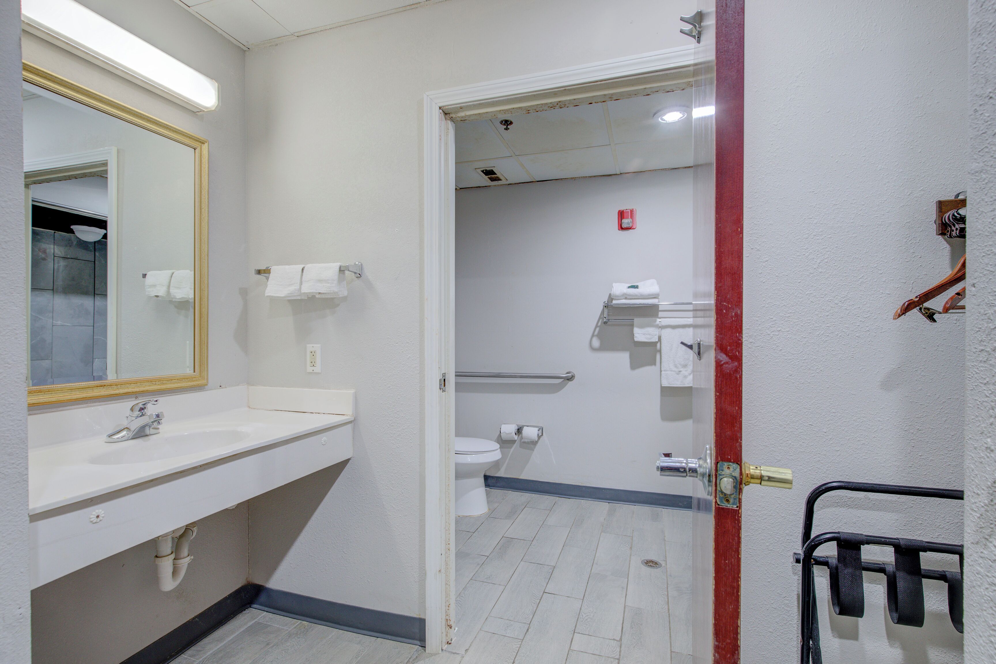 A bathroom with a white sink, mirror, and toilet. There is a towel rack and a shower area visible through the door.