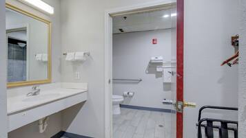 A bathroom with a white sink, mirror, and toilet. There is a towel rack and a shower area visible through the door.