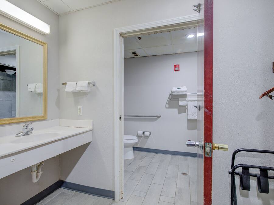 A bathroom with a white sink, mirror, and toilet. There is a towel rack and a shower area visible through the door.