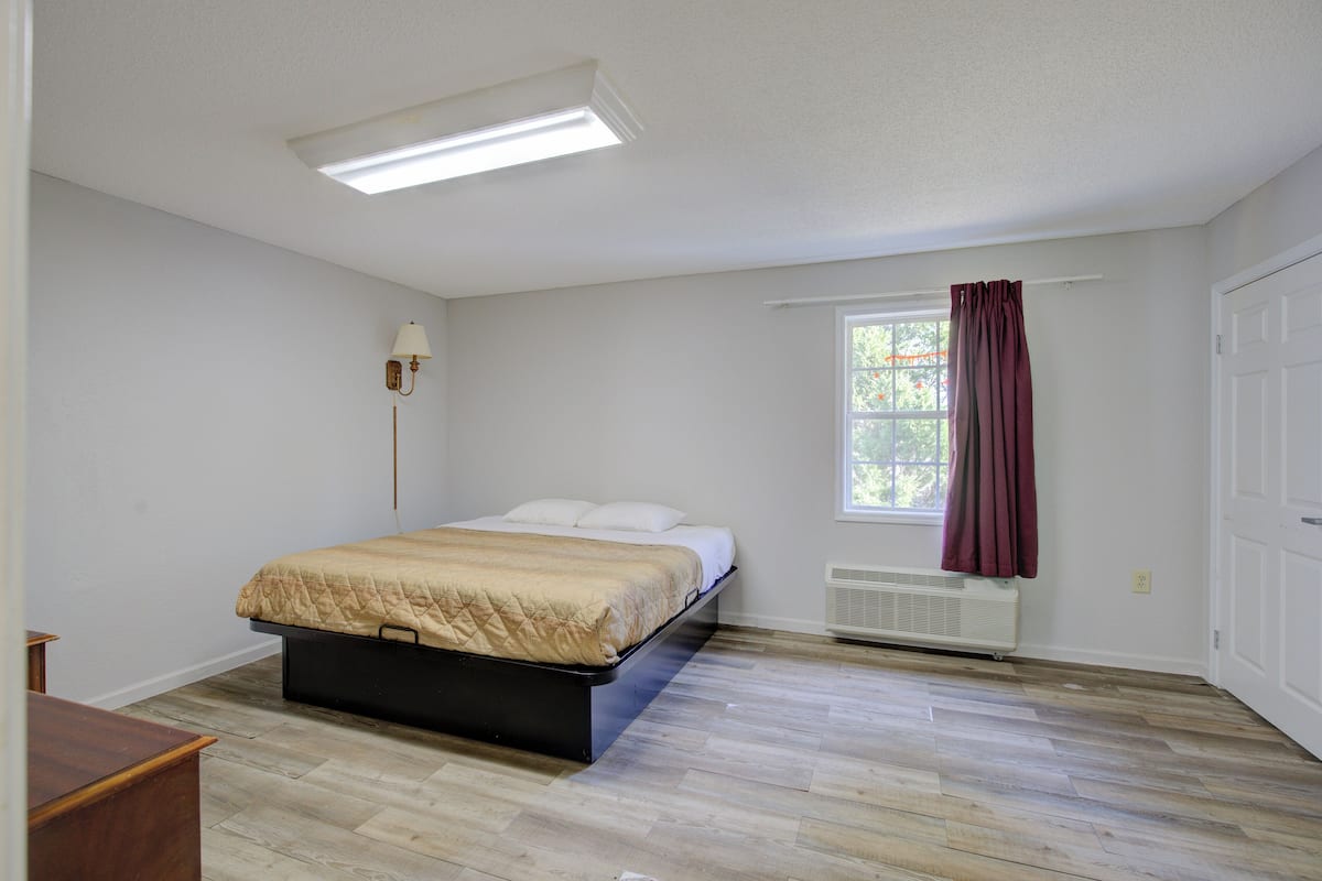 A bedroom with a bed, a window with curtains, a radiator, and a ceiling light.