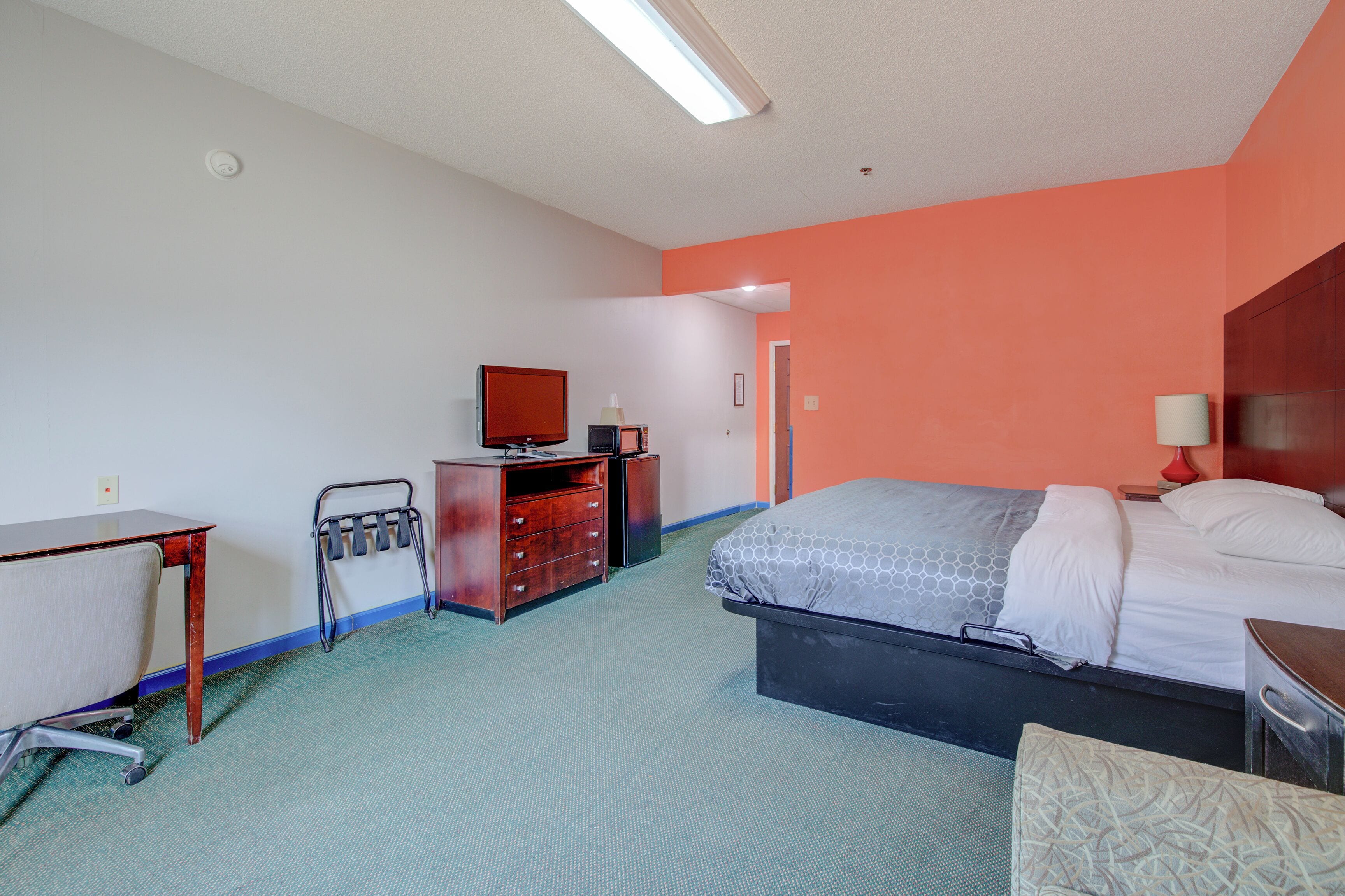 Ein Hotelzimmer mit Bett, Schreibtisch, Stuhl, Kommode, Fernseher und einer Badezimmertür.