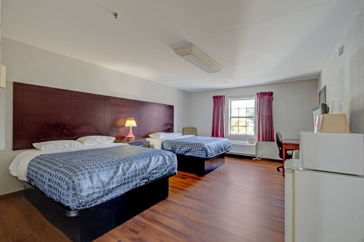 A hotel room with two beds, a desk, a chair, a lamp, and a window with curtains.