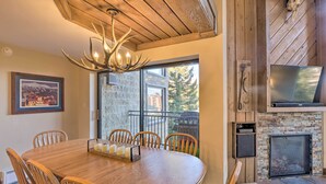 A dining area with a wooden table and chairs, a chandelier, a fireplace, and a television mounted on the wall. - Walk to Ski Lift: Mtn-View Condo in Breckenridge (Breckenridge)