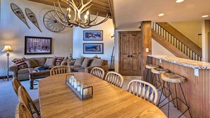A cozy living room with a wooden dining table, bar stools, and a chandelier. - Walk to Ski Lift: Mtn-View Condo in Breckenridge (Breckenridge)
