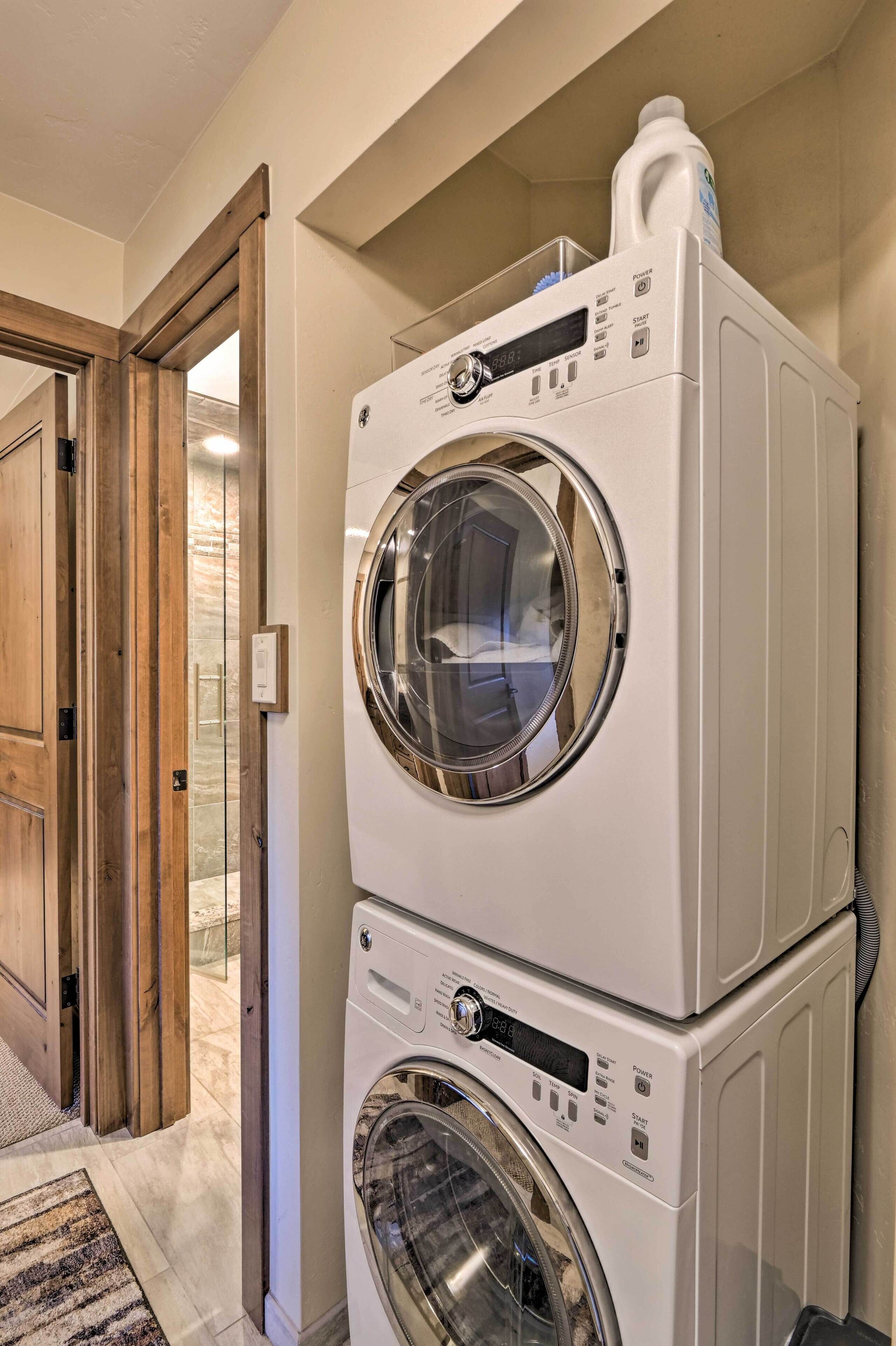 A stacked washer and dryer unit in a laundry room with a wooden door and a rug on the floor.