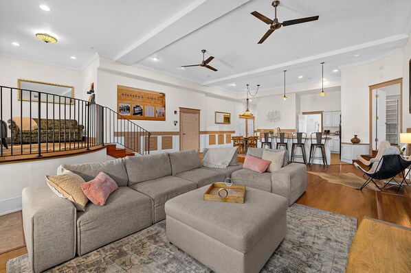 A spacious living area with a sectional sofa, a dining table, and a kitchen in the background.