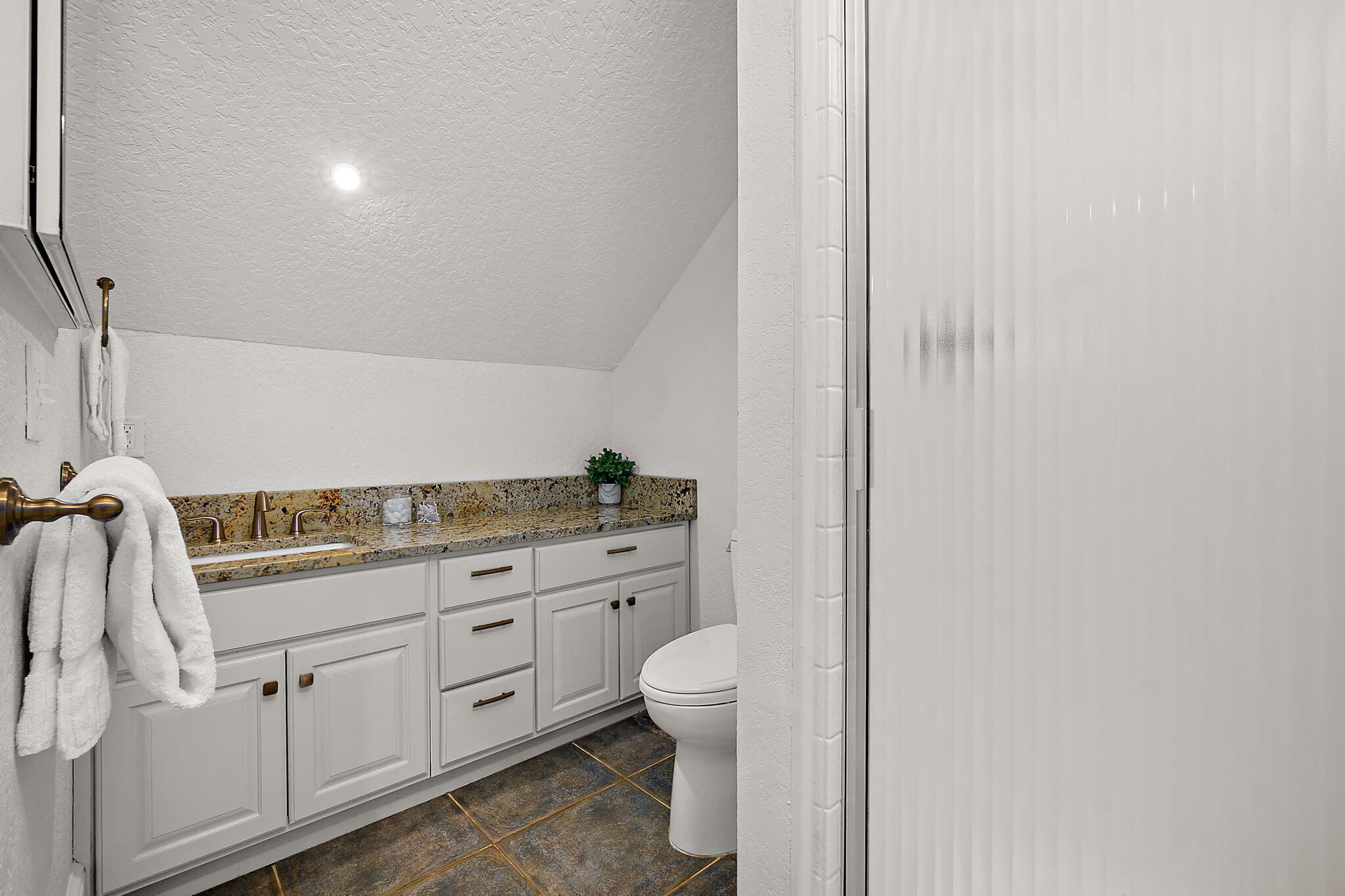 A bathroom with white cabinets, a granite countertop, a white toilet, and a shower area.