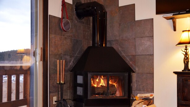 Una estufa de leña con chimenea, leños y fuego encendido en su interior.