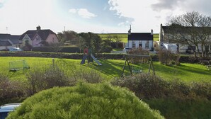 Un campo cubierto de césped con juegos infantiles, casas al fondo y un cielo despejado.