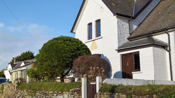 Una casa blanca de dos pisos con un muro de piedra, un gran árbol y una cerca de piedra.
