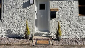 Une petite maison blanche avec une porte, une petite fenêtre et une pancarte indiquant « Terraughtie Cottage East ».