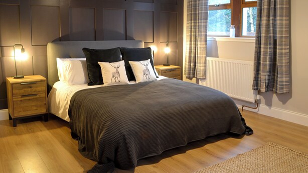 Une chambre avec un grand lit, deux tables de chevet, une tête de lit à panneaux, une fenêtre avec des rideaux et un radiateur.