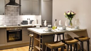 Une cuisine moderne avec des meubles gris, un four encastré, un plan de travail en marbre et des tabourets en bois.