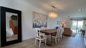 A dining area with a wooden table and white chairs, a large abstract painting, and a chandelier. - "Infinity Poolside" - Ocean Villa 2 BR / 3 BA  (Bimini)