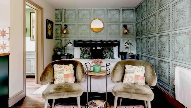 A bedroom with a bed, two chairs, a round table, and decorative wall panels. - Peaceful Studio Flat With Patio and Dogs Allowed (Cobham)