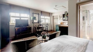 A compact hotel room with a bed, a desk, a chair, a TV, and a kitchenette. - Peaceful Studio Flat With Patio and Dogs Allowed (Cobham)
