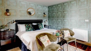 A bedroom with a large bed, two chairs, a nightstand, a dresser, and a patterned wallpaper. - Peaceful Studio Flat With Patio and Dogs Allowed (Cobham)