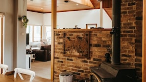 Un intérieur chaleureux avec une table à manger en bois, une cheminée en briques et une vue sur l’espace de vie.