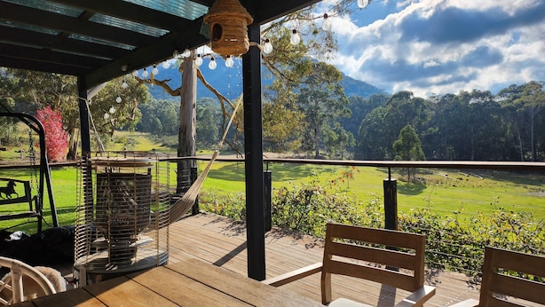 Une terrasse en bois avec un hamac, un banc et une vue sur un champ verdoyant et des arbres.