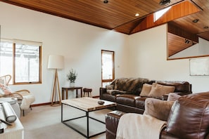 Ein geräumiges Wohnzimmer mit einem braunen Ledersofa, einem Holztisch und einem großen Fenster, das für natürliches Licht sorgt.