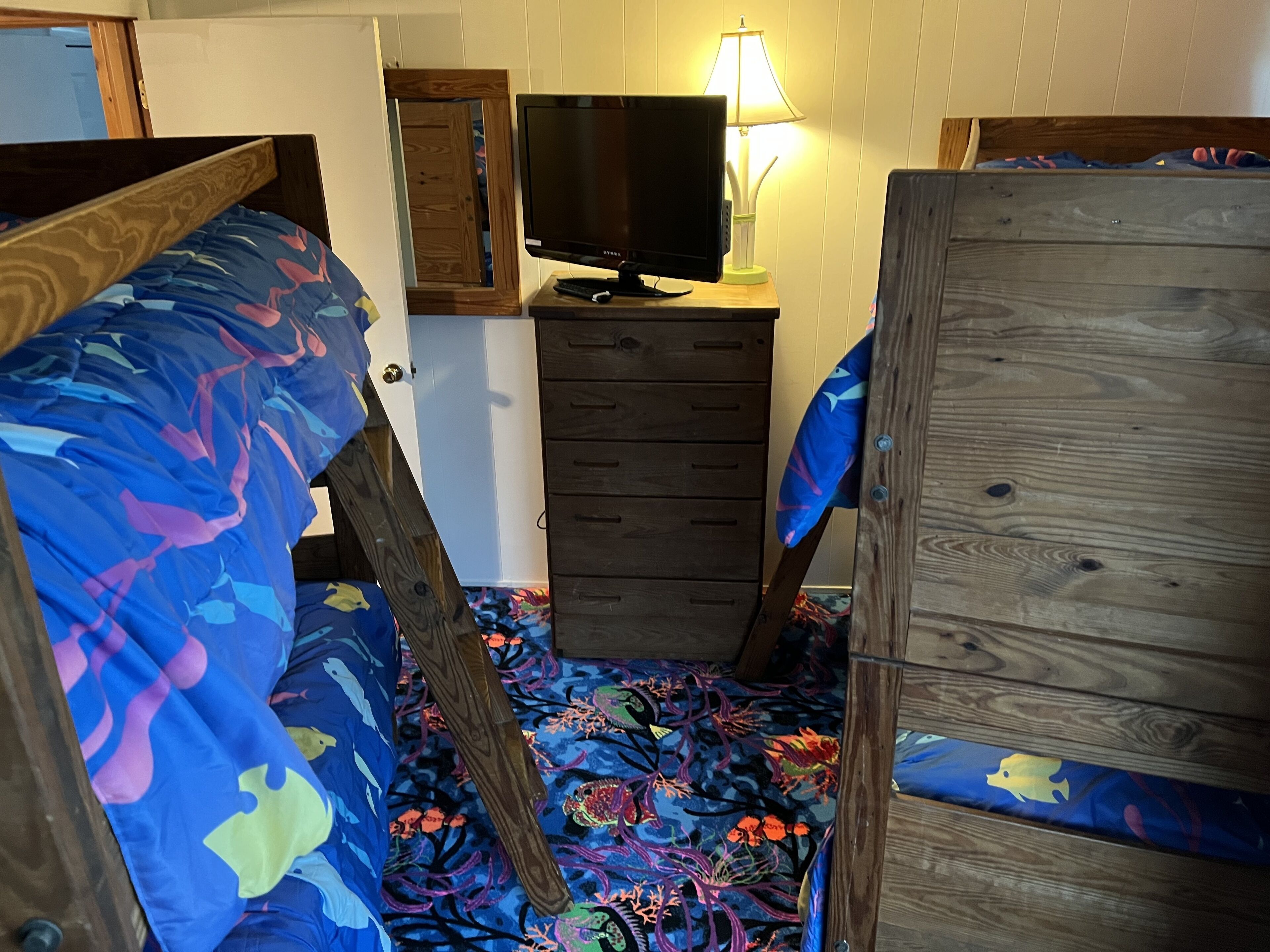 A room with bunk beds, a television, a dresser, and a lamp.