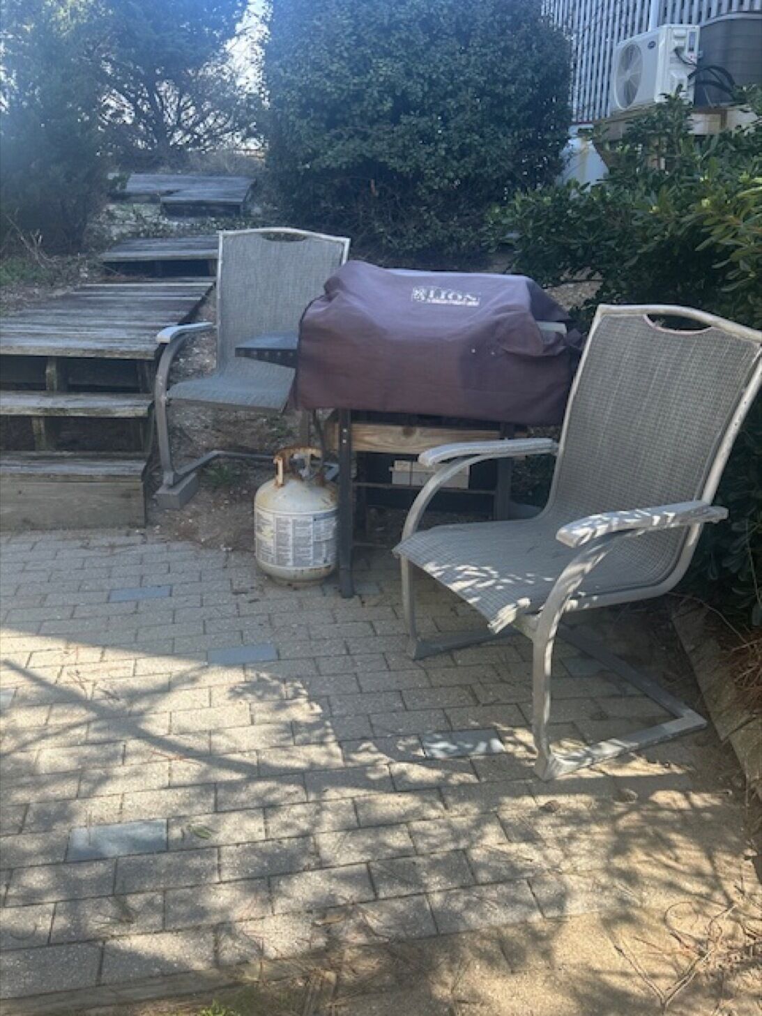 Une terrasse avec un barbecue, des chaises et une bouteille de propane.