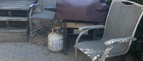 A patio with a grill, chairs, and a propane tank.