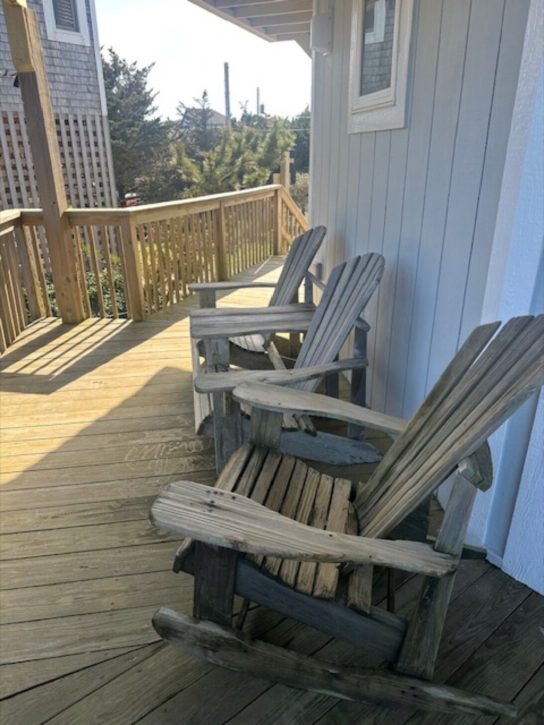 Una terraza de madera con sillas Adirondack y barandilla.