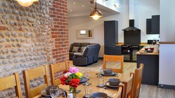 A dining area with a brick wall, a sofa, and a kitchen in the background.