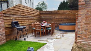 Un jardin avec une terrasse en bois, un jacuzzi, un barbecue et une table à manger avec des chaises.