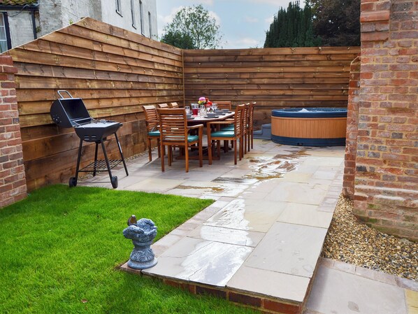 A backyard with a wooden deck, a hot tub, a barbecue grill, and a dining table with chairs.