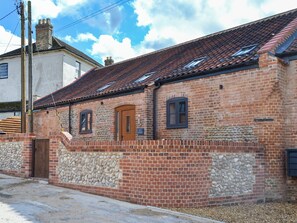 A traditional brick building with a stone wall, a wooden door, and a small window. - 4 bedroom accommodation in Swafield, near North Walsham (Swafield, near North Walsham)