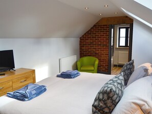 A bedroom with a sloped ceiling, a television on a wooden dresser, a green chair, and a bed with patterned pillows.