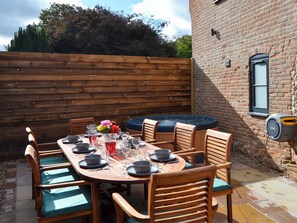 A wooden table set for six with chairs, a brick wall, and a hot tub in the background. - 4 bedroom accommodation in Swafield, near North Walsham (Swafield, near North Walsham)