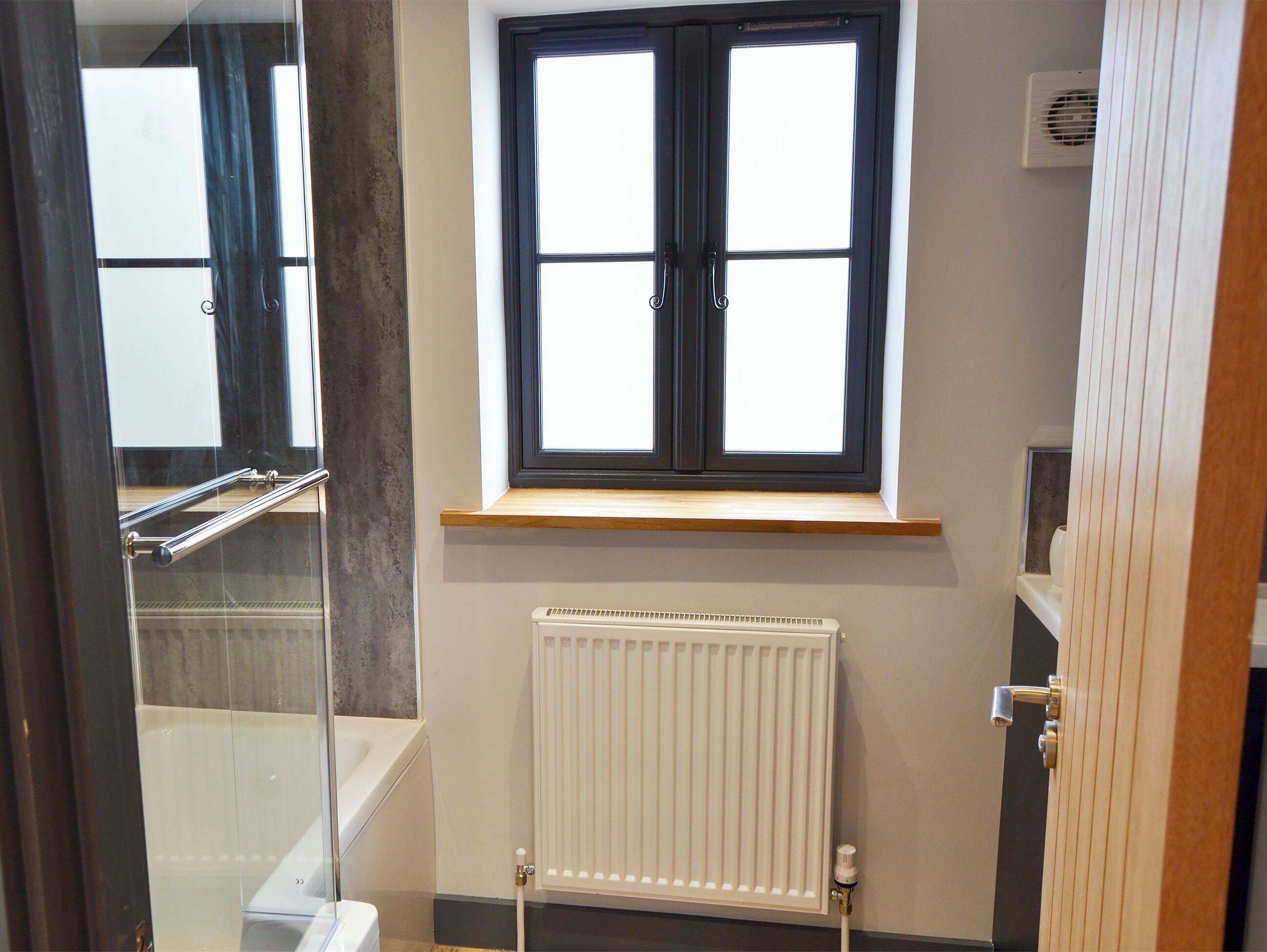 Ein Badezimmer mit Fenster, Heizkörper und einer Badewanne.