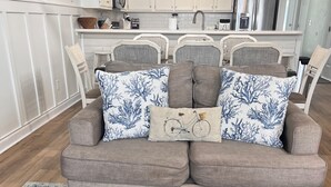 A living room with a grey sofa, patterned cushions, and a coffee table with seashells. - 'Off The Deck', Newly renovated! Steps away from the beach and entertainment!  (Surfside Beach)