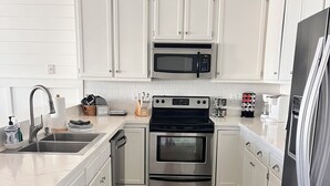 A modern kitchen with white cabinets, stainless steel appliances, a built-in microwave, and a coffee maker. - 'Off The Deck', Newly renovated! Steps away from the beach and entertainment!  (Surfside Beach)