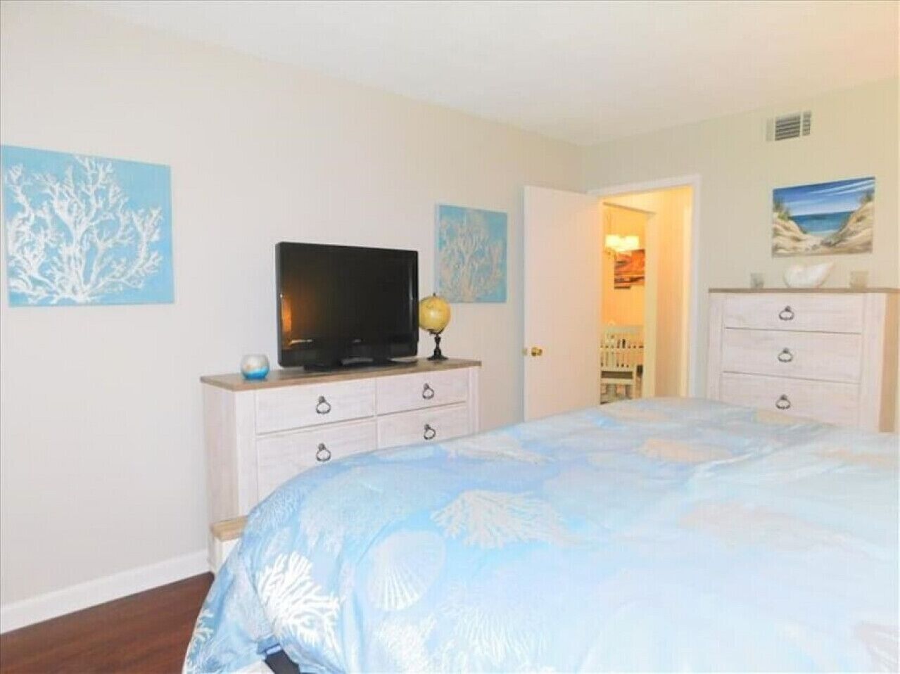 A bedroom with a bed, a television on a dresser, and artwork on the walls.