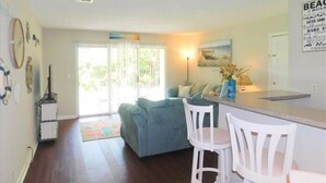Una sala de estar con un sofá, un comedor con mesa y sillas, y una zona de cocina con mostrador y refrigerador.