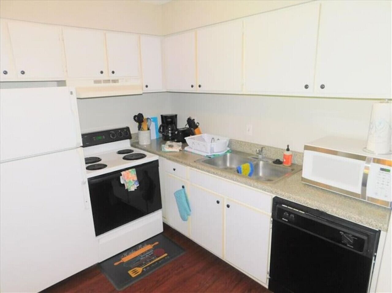 A compact kitchen with white cabinets, a stove, a microwave, and a dishwasher.