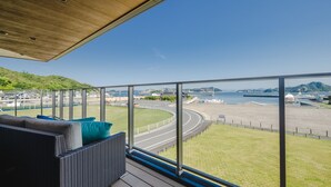 Ein Balkon mit Blick auf eine Küstenstraße, Grünflächen und ein Gewässer.