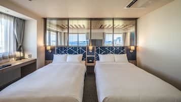 Ett hotellrum med två sängar, ett skrivbord och utsikt över stadsbilden.