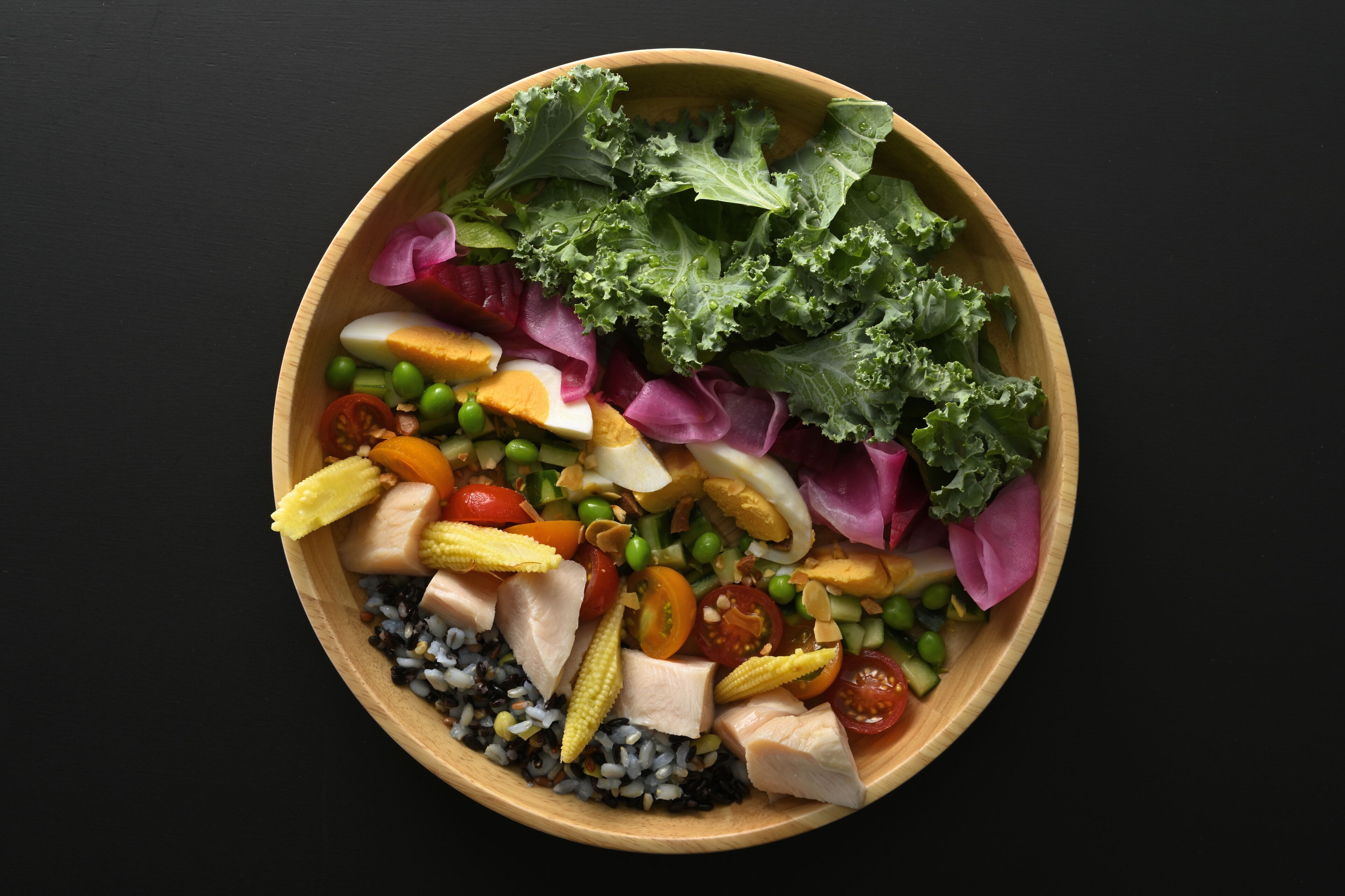 Un tazón de madera lleno de una ensalada colorida con lechuga, tomates, maíz y otras verduras.