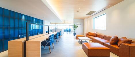 Un espacio de oficina moderno con un escritorio de madera largo, sillas azules, un sofá de cuero marrón y un ventanal grande.