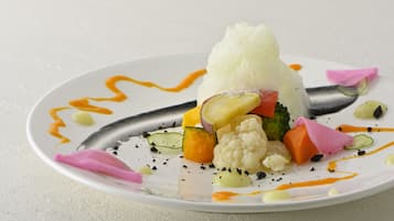A white plate with a variety of vegetables and a white dessert, possibly ice cream, on a textured surface.
