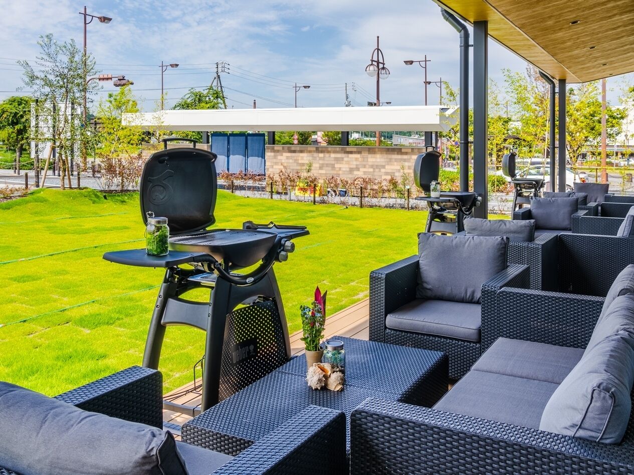 An outdoor patio area with a grill, seating, and a view of the surrounding greenery and buildings.