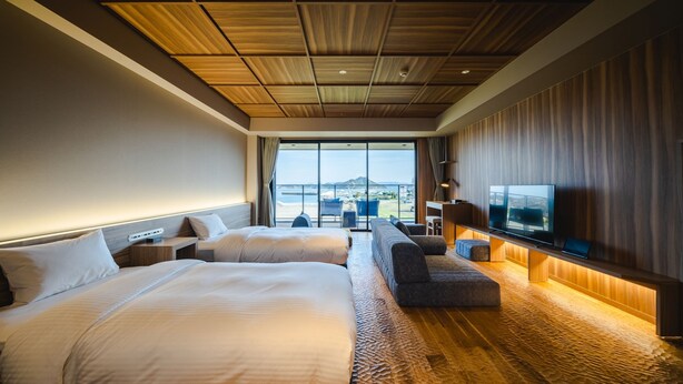 Ein modernes Hotelzimmer mit zwei Betten, einem Sofa, einem Fernseher und Blick auf den Strand.