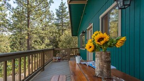 Une terrasse en bois avec une table et un vase rempli de tournesols, le tout entouré d’arbres.