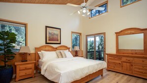 Une chambre à coucher avec un lit en bois, deux tables de chevet, un grand miroir et un ventilateur de plafond.